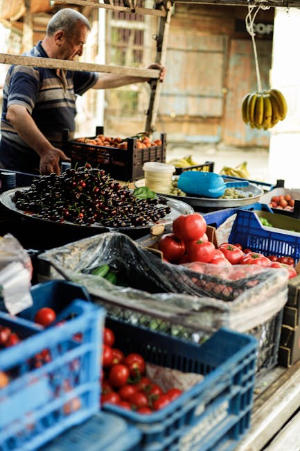 A woman with dark hair, wearing a dark grey t-shirt and mint green shorts, stands with her back to the camera, browsing a market stall that is set up on the back of a small truck. The stall displays a